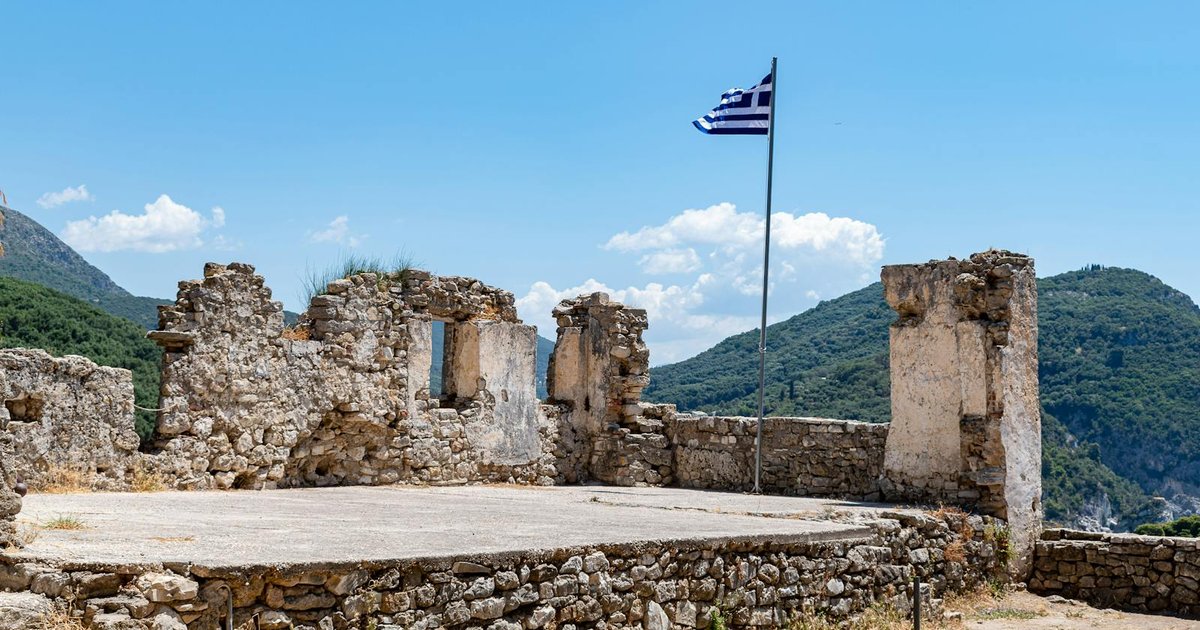 Ancient stone ruins among olive trees with the Ionian Sea in the background